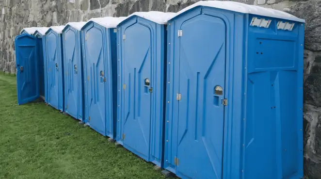 Row of blue portable toilets lined up on grass against a stone wall for event sanitation in Tucson, AZ